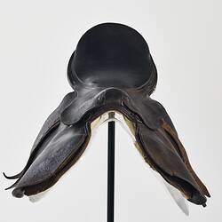 Horse racing saddle. Padded dark brown leather. Double layer beneath saddle flap. Two leather straps on either side. Back view.