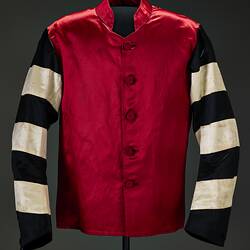Red riding jacket with red buttons. Black and white hoops on sleeves. Short stand up red collar. Black background.