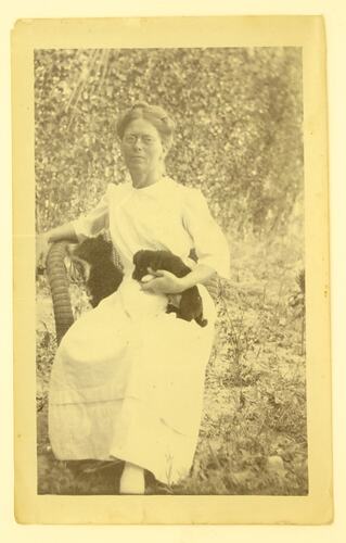 seated woman holding two black puppies.