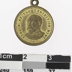 Round gold coloured medal with profile of man and text surrounding.