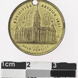 Round gold coloured medal with building, text surrounding.