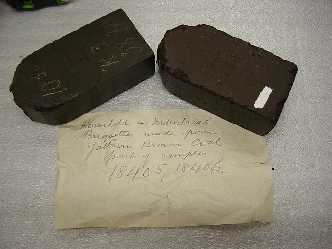 Two black chipped and worn sections of a briquette.