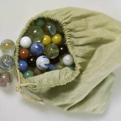 Coloured glass marbles in light green cloth bag.