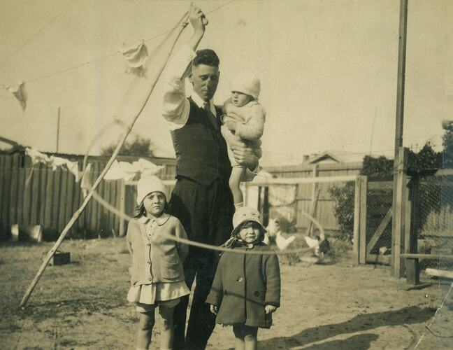 Man spinning the rope around himself and three children in suburban backyard, Footscray, c. 1925