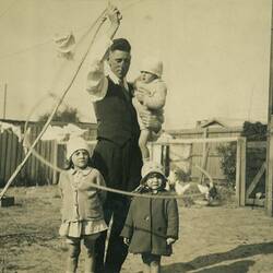 Man spinning the rope around himself and three children in suburban backyard, Footscray, c. 1925