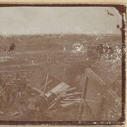 Group of soldiers in front of destroyed building, muddy landscape in background.