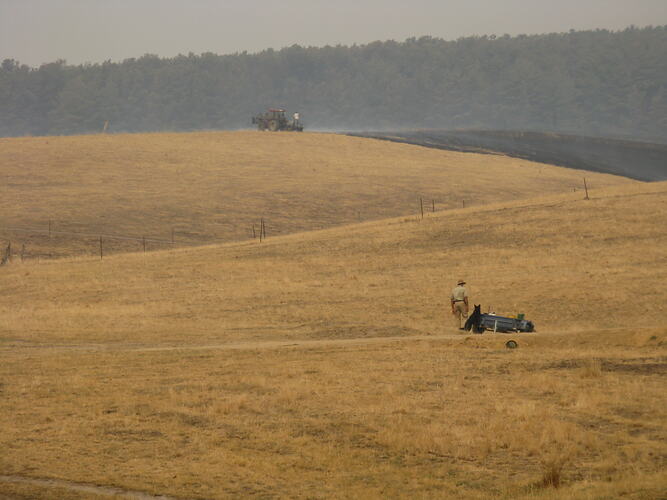 Man on tractor putting out bushfire on hillside.