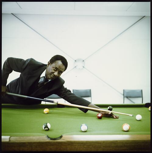 Man in uniform with tie and jacket playing billiards.