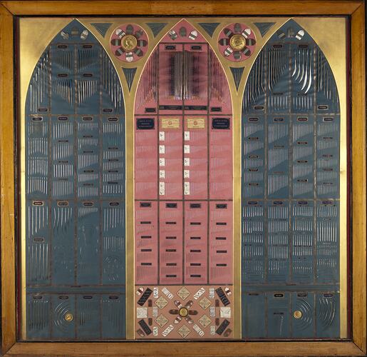 Three Gothic window-style arched panels made of needles, crochet hooks, surgical needles, and other needles and needle cases. In red, black and yellow.