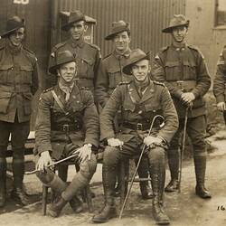 Group of seven servicemen, two seated and five standing, with building behind.