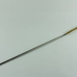Metal rod-like cleaning tool with narrow brush at end.