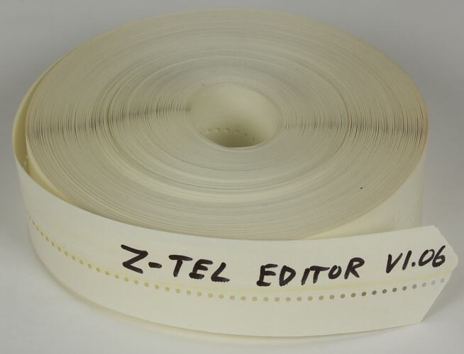 White reel of paper punched tape with balck handwriting.