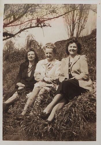 Three women seated on grassy slope.