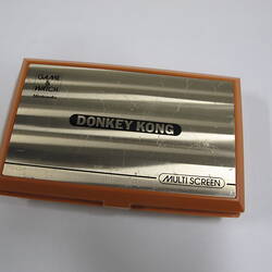Orange plastic, handheld game console, rectangular, closed. Hinge at top. Front has metallic label and text.