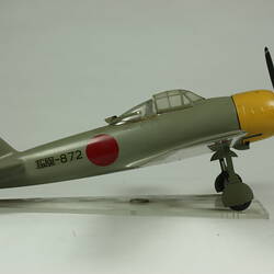 Green grey plane model with red spot on each wing and fusleage. Yellow nose, black propeller. Profile.