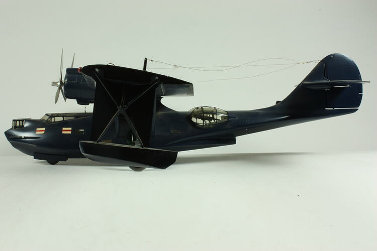 Navy twin propeller aeroplane model with three wheels. Red and white flags affixed near cockpit.