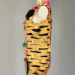 Left side of dress made of horizontal strips of pink, yellow, blue plastic. Adorned with plastic cables, dolls