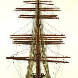 Rear view of three masted ship with red hull.