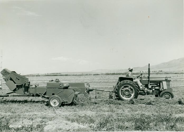 A man driving a tractor with a baler with bale thrower fitted.