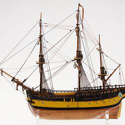 Wooden ship model with varnished hull, yellow and black painted quarters and rudder, and three masts with rigg