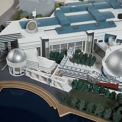 Detail of cardboard model of building with two silver domes and curved steps leading down to river.
