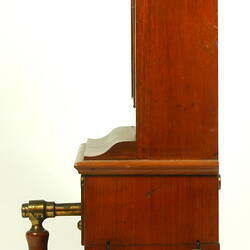 Wooden cabinet with wooden handle at base. Left profile shows two round brass discs near base.