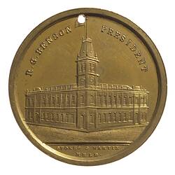 Medal with Malvern Town Hall. View of two-storey corner building with tower. Text above and below.