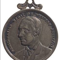 Round silver medal with bust of man facing left. Text around edge and  decorative loop at top.
