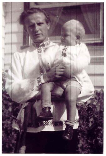 Man holding child (toddler) both wearing white embroidered shirts.