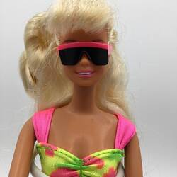 Blonde Barbie doll. Wears pink strapped multi-coloured bikini top and sunglasses.