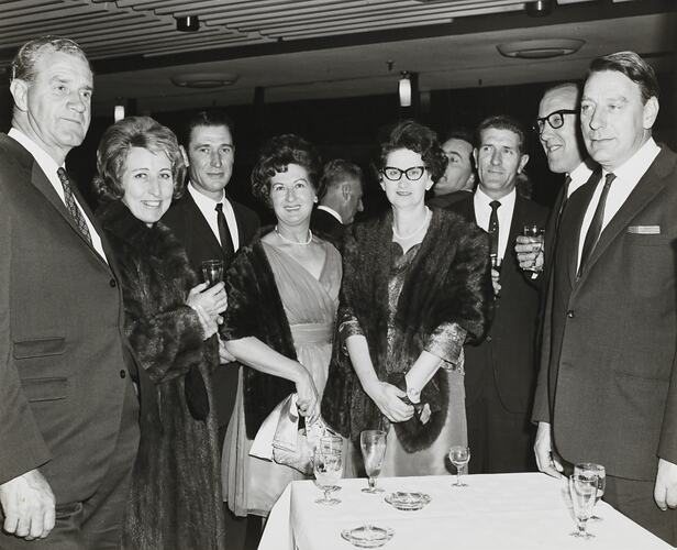 Men and women in formal dress standing behind a table at a Massey Ferguson's social function.