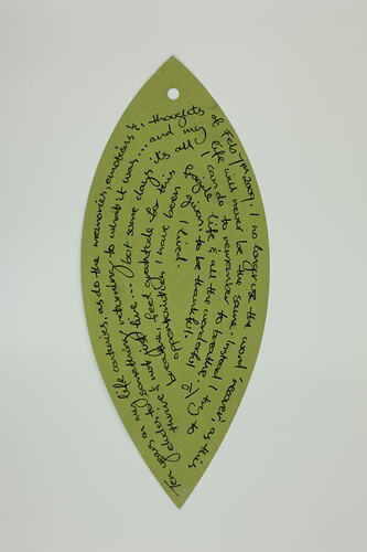 Green paper leaf with handwritten text in black ink.