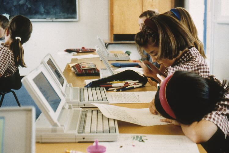 Two young girls in school uniform with laptops.