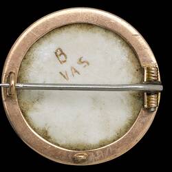 Back of round white porcelain brooch with gold border and horizontal pin. B and VAS on porcelain.