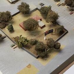 Model detail, aerial view of red-roofed building surrounded by trees. Carpark around it.