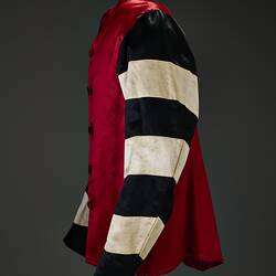 Profile of red riding jacket with red buttons. Black and white hoops on sleeves. Short stand up red collar. Black background.