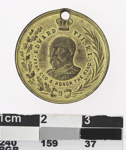 Round gold coloured medal with crowned profile of man, with text and wreath surrounding,