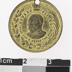Round gold coloured medal with crowned profile of man, with text and wreath surrounding,