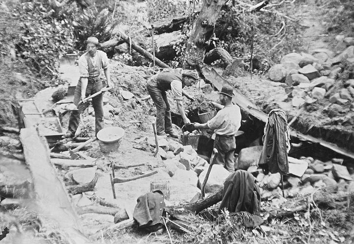 Miners using a sluice in a rocky setting.