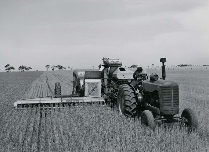 Man driving a tractor coupled to a Header Harvester.
