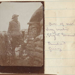 Two soldiers in snow covered trench, man on left inside sandbag structure with only head visible.