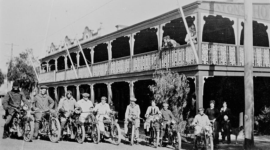 Motorcycle riders sitting on their motorcycles outside a double storey hotel with an ornate verandah and balcony.