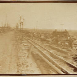 Dirt road and railway track with wreckage of a train on the ground.