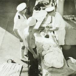Sailors on a ship wrapping a body in cloth.