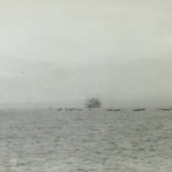 Multiple barges and two ships in open water in the background.
