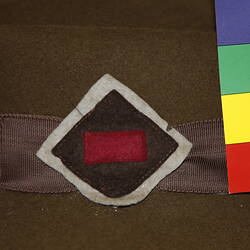 Felt patch with white diamond, topped with brown diamond, topped with maroon rectangle sewn onto hat band.