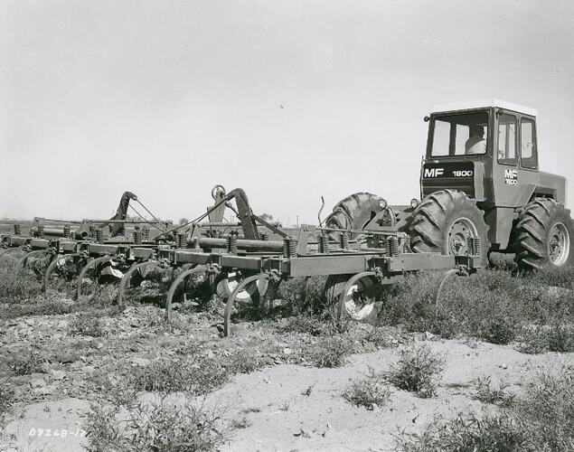 Man driving a tractor coupled to a large wide folding cultivator.