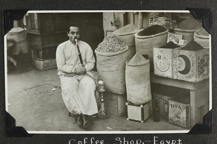 Man sitting in front of sacks and boxes of food items smoking a hookah.