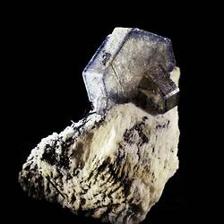 Clear white and blue hexagonal crystals on a creamy block of mineral.