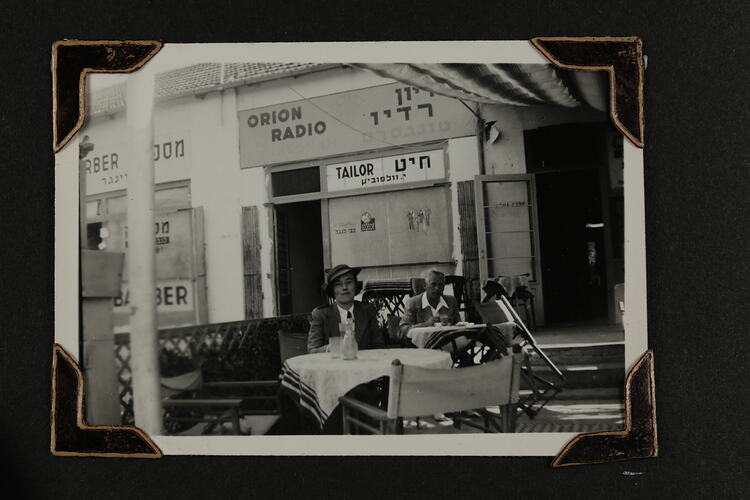 Woman and man sitting at two separate café tables in front of building.